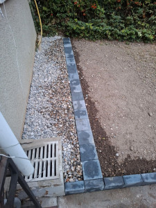 Photo de galerie - Pose d une bordure en pavé béton et mise en place  de cailloux sur une bache  pour effectuer une banquette de propreté le long  du mur 