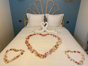 Photo de galerie - Préparation d’une chambre avec décoration romantique incluant pétales de fleurs en cœur et pliage décoratif de serviettes.