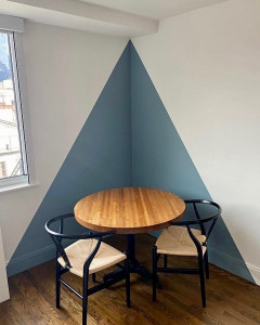 Photo de galerie - Création d'un angle décoratif géométrique en peinture bleu-gris (y compris les plinthes) sur fond blanc pour structurer un coin repas avec des lignes parfaitement nettes.
