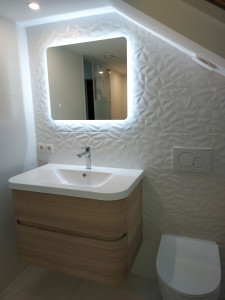 Photo de galerie - Pose de carrelage mural 3D dans une salle de bain moderne, avec finitions soignées autour du meuble vasque et du miroir rétroéclairé. Un rendu élégant et contemporain qui apporte luminosité et style à l’espace