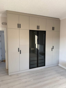 Photo de galerie - Fabrication et pose d’un dressing sur mesure avec portes vitrées, tiroirs intégrés et finitions soignées.