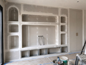 Photo de galerie - Création d’un aménagement mural sur mesure comprenant niches décoratives méditerranéennes, emplacement TV intégré et futur meuble bas de rangement.