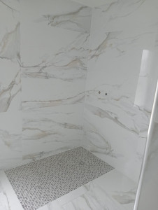 Photo de galerie - Douche habillée de carrelage grand format imitation marbre blanc aux veinages gris et beige. Le sol en mosaïque gris clair apporte contraste et sécurité. L’ensemble offre un rendu moderne, lumineux et élégant.