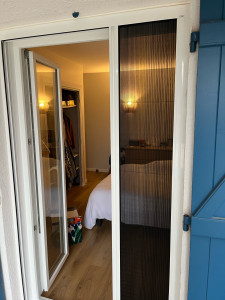 Photo de galerie - Porte-fenêtre 2 vantaux en PVC blanc,  Vitrage clair offrant une belle luminosité. Présence d’une moustiquaire non intégrée, installée en complément pour permettre l’aération tout en protégeant contre les insectes. Idéale pour un accès terrasse ou balcon.