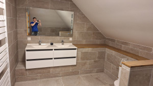 Photo de galerie - Salle de bain élégante et contemporaine, avec carrelage effet pierre, meuble suspendu à double vasque, plan en bois et finitions de qualité.