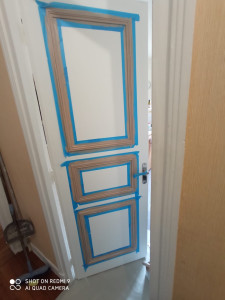 Photo de galerie - Préparation minutieuse d'une porte avant peinture, avec bandes de masquage pour un travail précis et propre.
