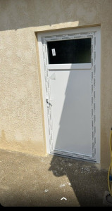 Photo de galerie - Fermeture d'une ancienne porte de garage type bois en agglo pour accueillir une porte de service type PVC . Réalisation d'un enduit temps pierre lissé.  