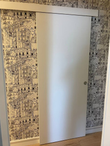 Photo de galerie - Pose d'une porte coulissante intérieure suspendue avec rail apparent : fixation du rail au mur, ajustement de la porte, réglage du mécanisme de coulissement. Solution gain de place pour cloison existante.