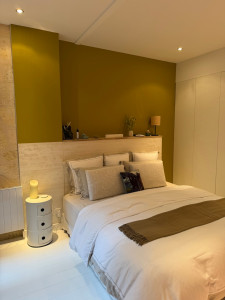 Photo de galerie - Après : Conseil et changement de coloris pour une teinte plus chaleureuse • Pose d’une tablette en chêne sur la tête de lit • Home staging et réorganisation de la décoration • Mise en valeur de l’ensemble de la pièce. 