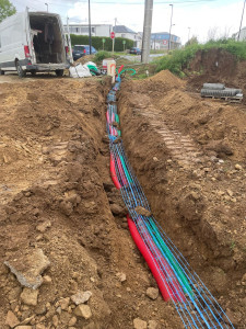 Photo de galerie - Réalisation de tranchées techniques pour réseaux électriques et télécom.
Pose de gaines rouges, vertes et bleues avec grillage avertisseur.