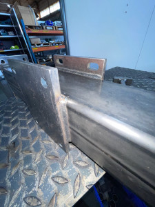 Photo de galerie - Assemblage acier avec platines percées soudées sur tube rectangulaire. Cordons réguliers, alignement précis et finition propre garantissant une fixation solide et durable pour pièces métalliques sur mesure.