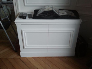 Photo de galerie - Meuble hifi reprenant les moulures, la plinthe et la couleur de la peinture du mur sur lequel il est adossé. Le meuble est composé de deux portes battantes et d'étagères réglables.